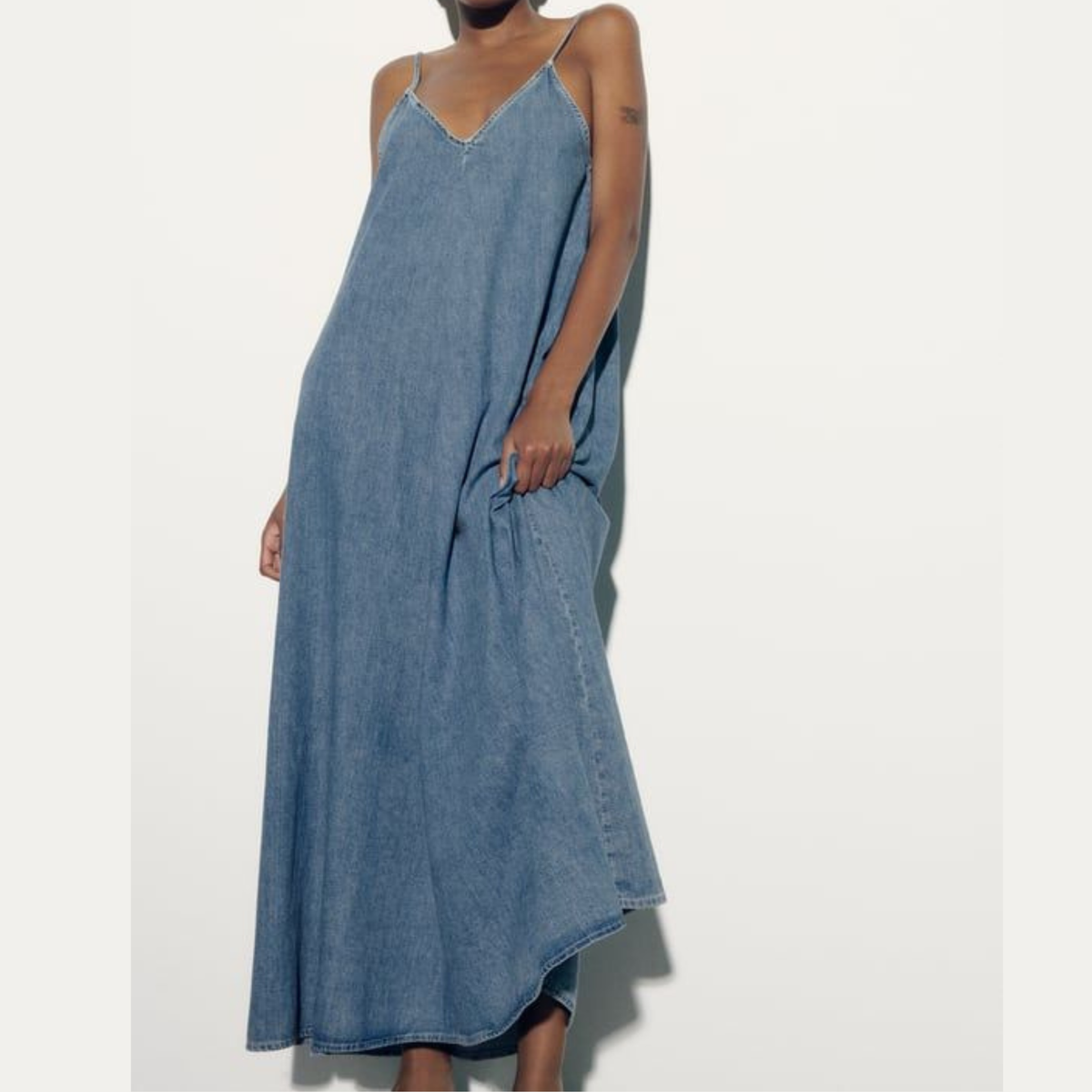 A model wearing a loose, midi-length Zara denim slip dress with thin spaghetti straps and side pockets from Closet Concierge