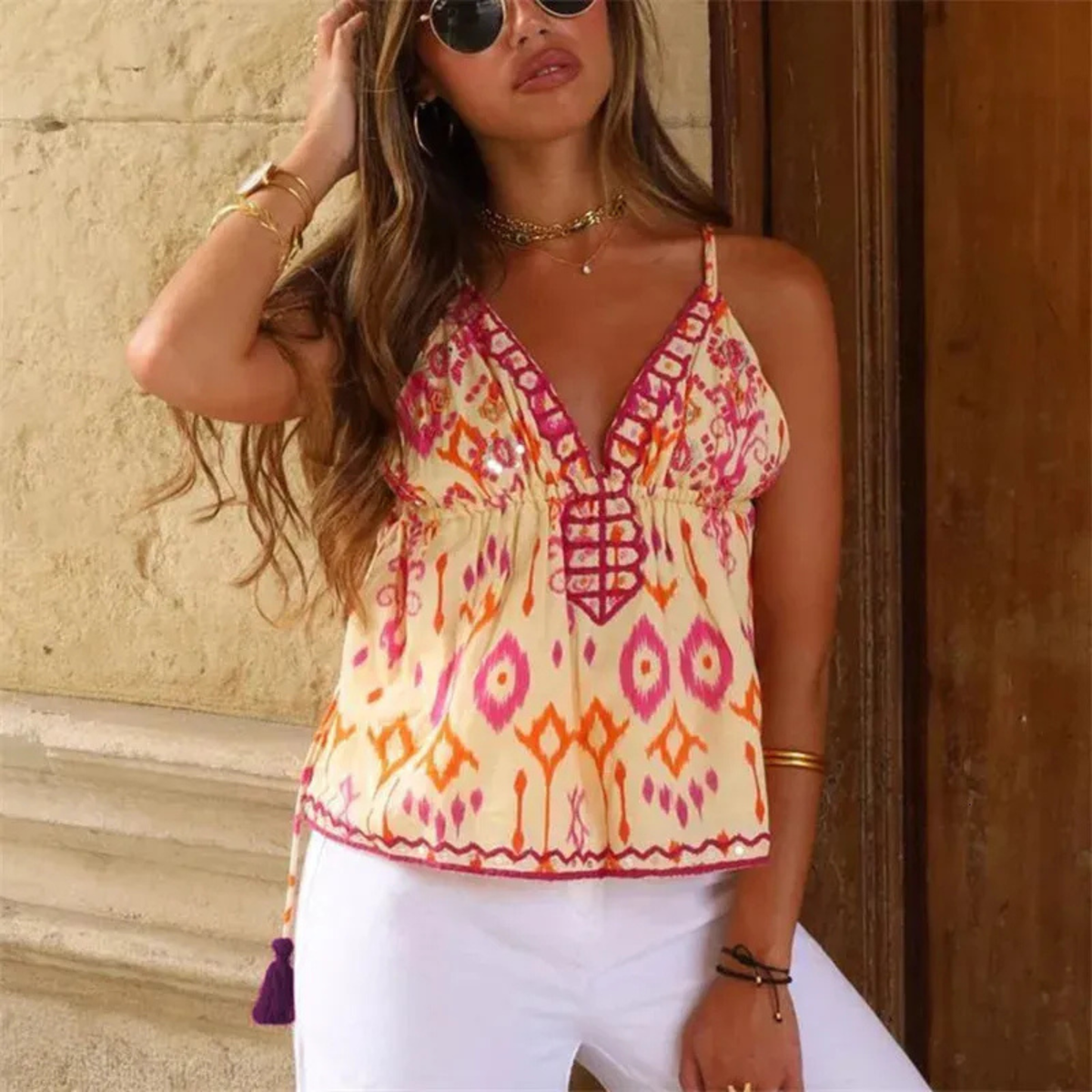 A woman wearing a Zara sleeveless bohemian-style camisole top with a cream base and pink, orange, and purple geometric ikat patterns, paired with white pants and sunglasses. From Closet Concierge.