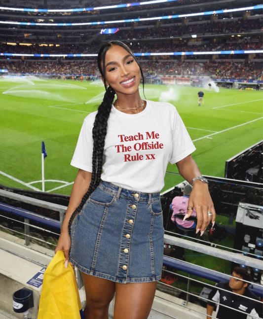 Woman in a stadium wearing a white t-shirt with text teach me the offside rule from closet concierge. 